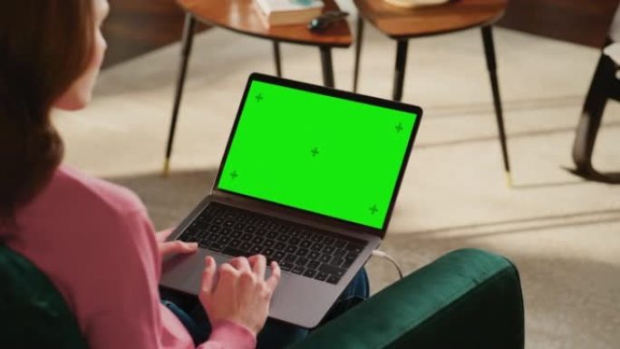年轻的成年女性在带绿屏模拟显示的笔记本电脑上的家庭阁楼公寓工作。有创造力的女性浏览网络，在社交媒体上