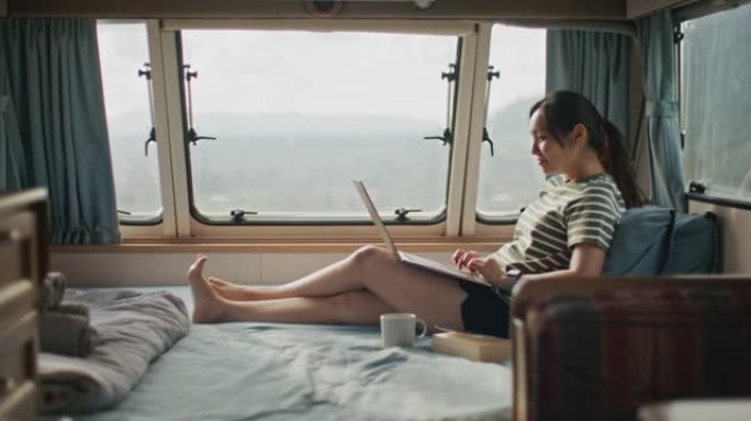 年轻女子在露营车的床上使用笔记本电脑