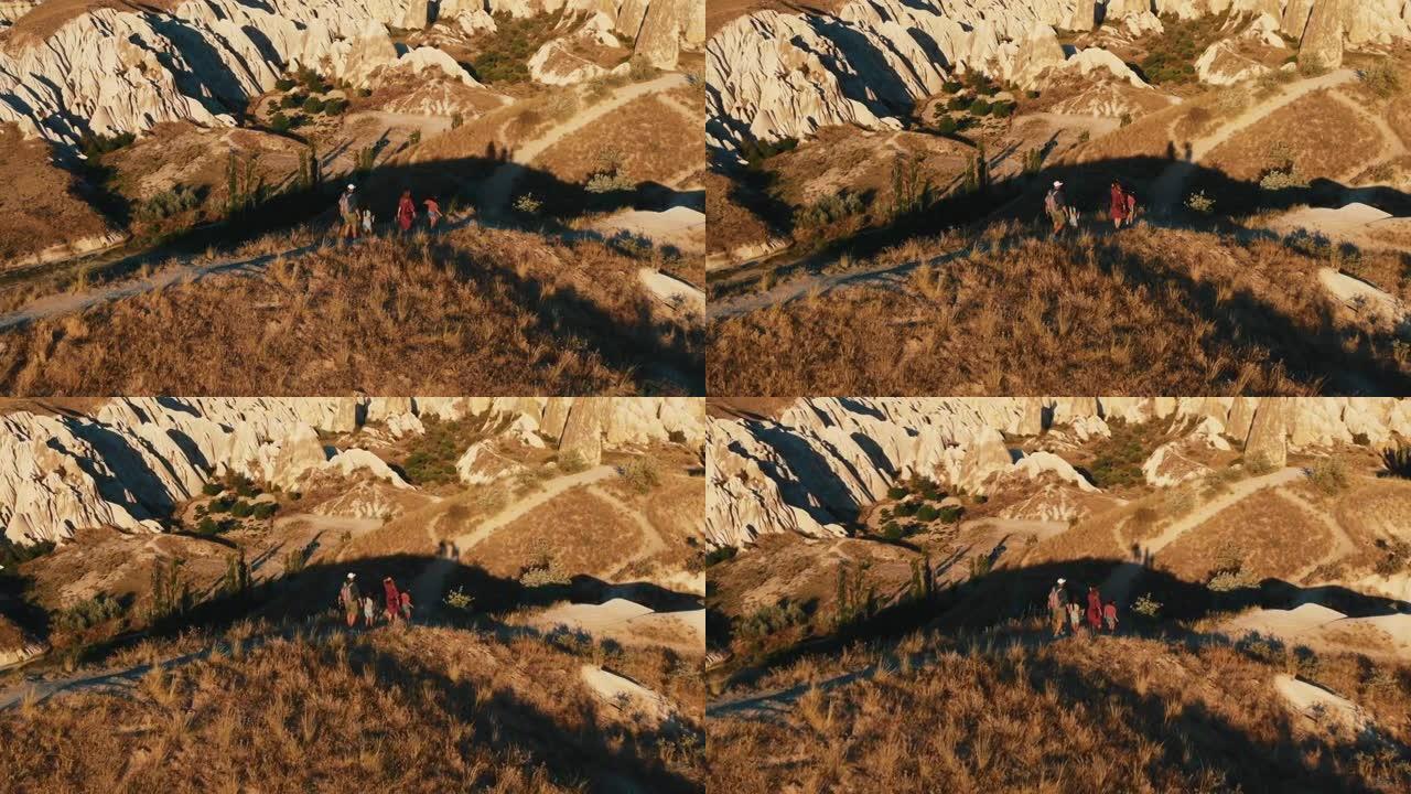 家庭徒步旅行鸟瞰男人、女人和两个孩子在阳光明媚的岩石上沿着美丽的小路行走，享受卡帕多西亚。