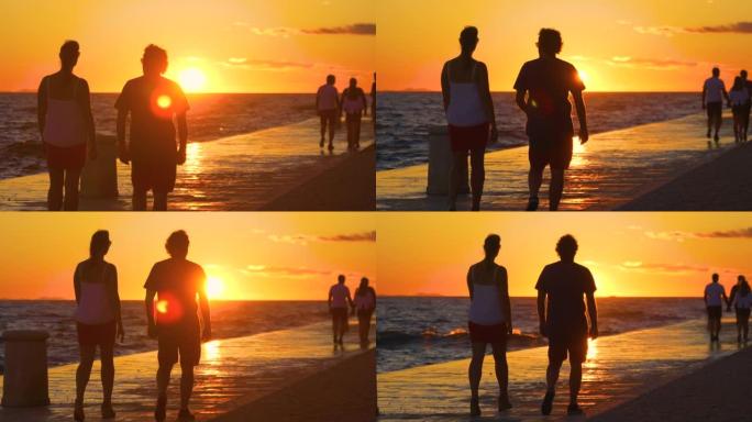 剪影: 年轻的女人和男人在日落时沿着风景秀丽的海滨散步。
