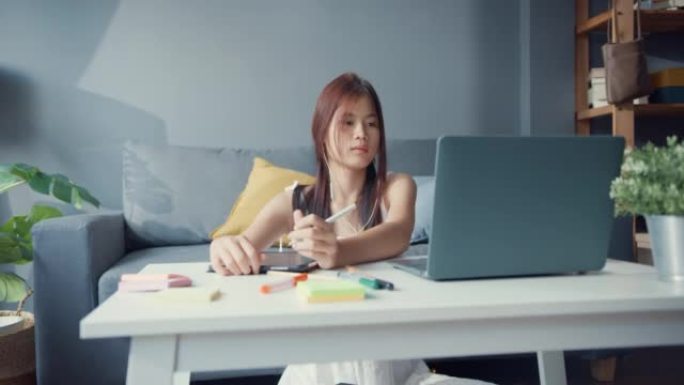 年轻的亚洲女孩青少年穿着休闲衬衫穿耳机使用笔记本电脑在线学习在家里的客厅笔记本电脑上写讲座。隔离教育