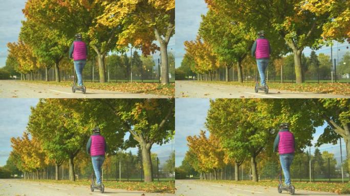 一名老年妇女在秋天的树木旁驾驶电动踏板车的后视图
