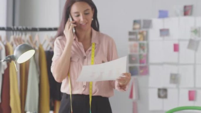 在手机通话中使用卷尺的女性时装设计师讨论在工作室工作的设计