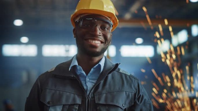 快乐专业的重工业工程师/工人，穿着制服，戴着眼镜，戴着安全帽在钢铁厂。微笑的非洲裔美国工业专家站在金