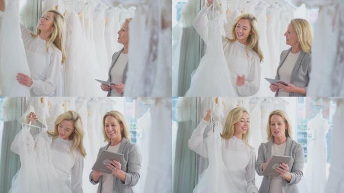 销售助理或商店老板用数字平板电脑帮助新娘商店的女人选择婚纱-慢动作拍摄