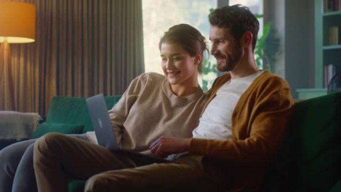年轻夫妇坐在舒适时尚公寓的沙发上，使用笔记本电脑。男女朋友在网上购物，观看有趣的视频和流媒体服务。中