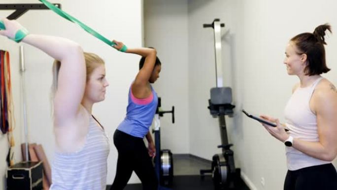两名妇女在健身房与健身教练一起进行阻力带锻炼