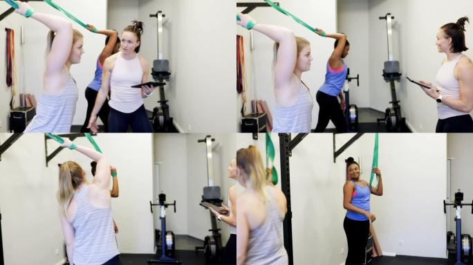两名妇女在健身房与健身教练一起进行阻力带锻炼