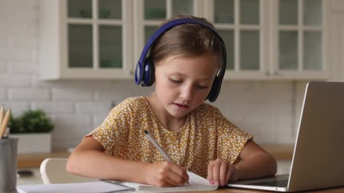 女学生戴着耳机听笔记本电脑上的音频写在抄本上