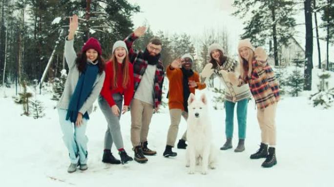 一起度假的朋友。一群多民族快乐的青年挥舞着，在白雪皑皑的森林慢动作中对着镜头微笑。