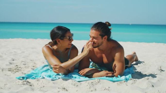 幸福的年轻夫妇的慢动作很有趣，可以在海滩度假期间涂上防晒霜或晒黑乳液来照顾他们的皮肤。