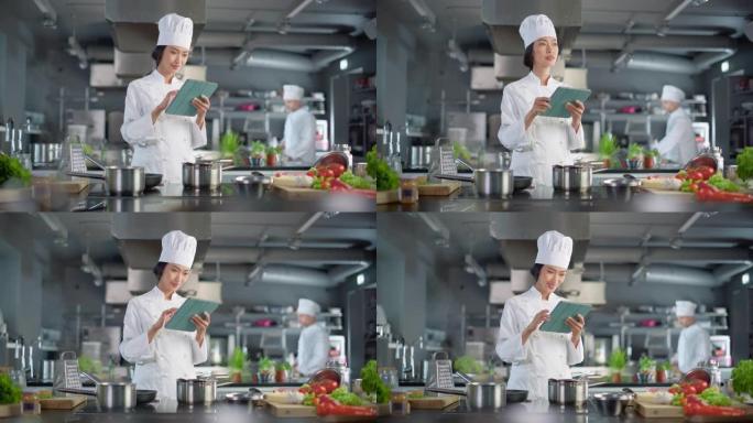 世界著名餐厅: 亚洲女厨师烹饪美味正宗的食物，在现代专业厨房工作时使用数字平板电脑。准备美味的有机菜