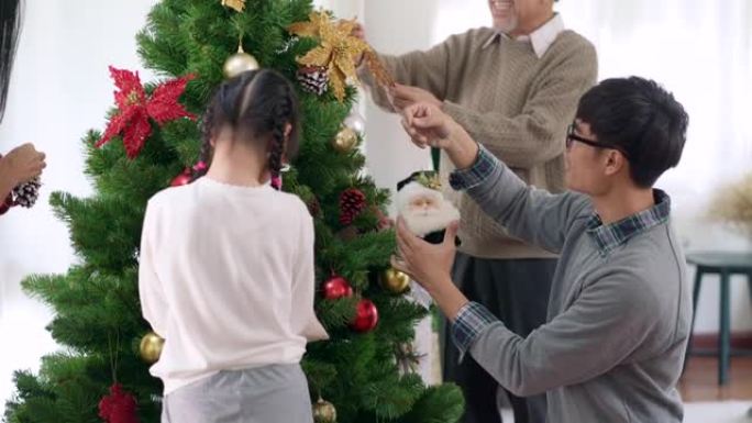 4K UHD倾斜多代亚洲幸福家庭装饰圣诞树与装饰品一起为节日快乐冬天做准备。