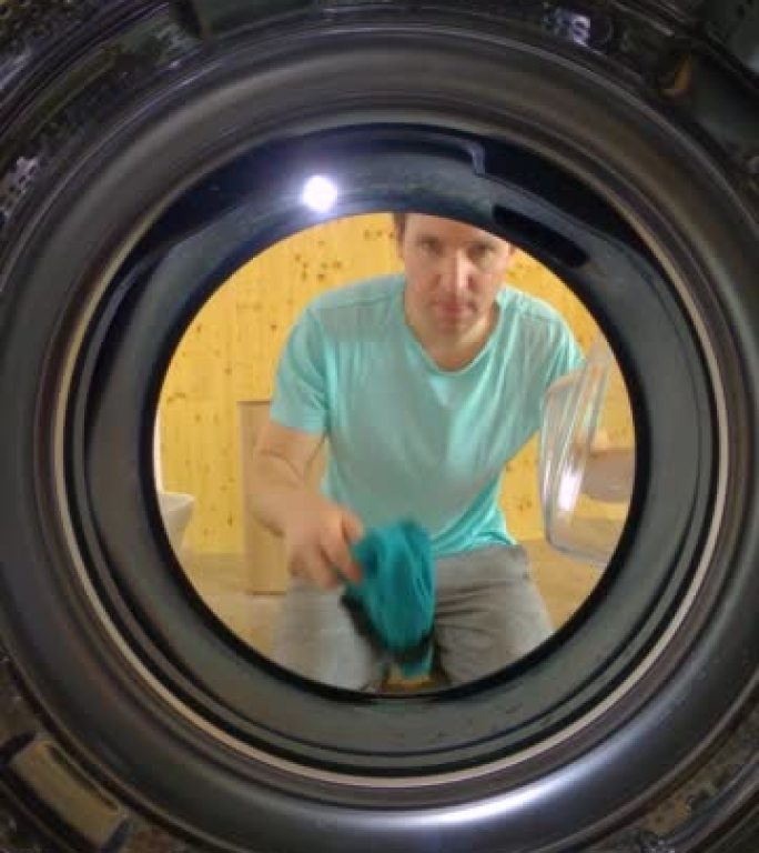 垂直，肖像: 男人把洗衣机装上，看着它洗脏衣服。