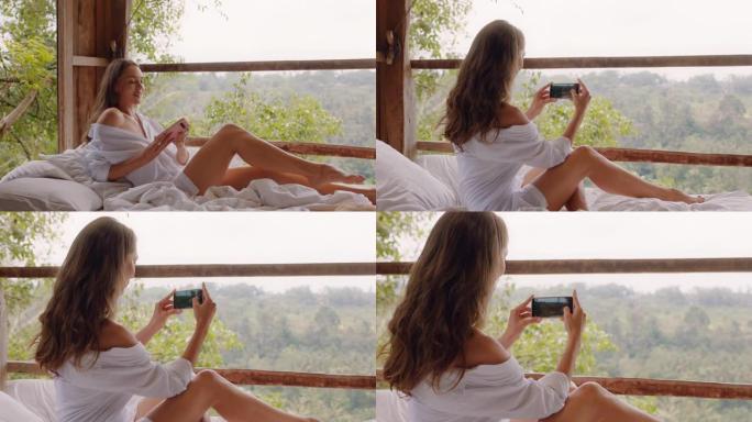 酒店度假村床上使用智能手机拍摄热带丛林照片，用手机在线分享异国度假