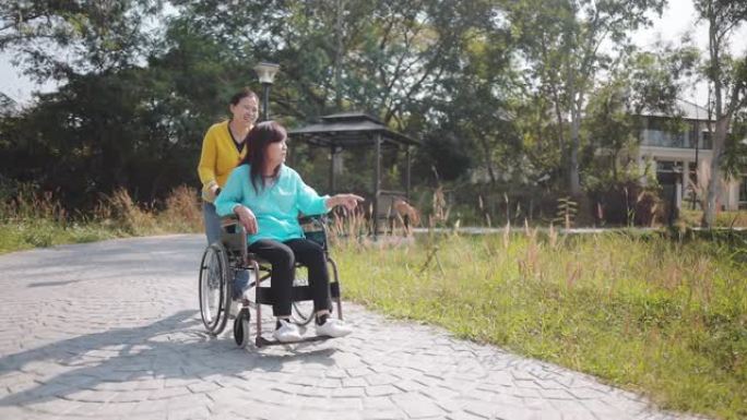 快乐微笑的母亲坐在轮椅上放松和与女儿在公园户外散步