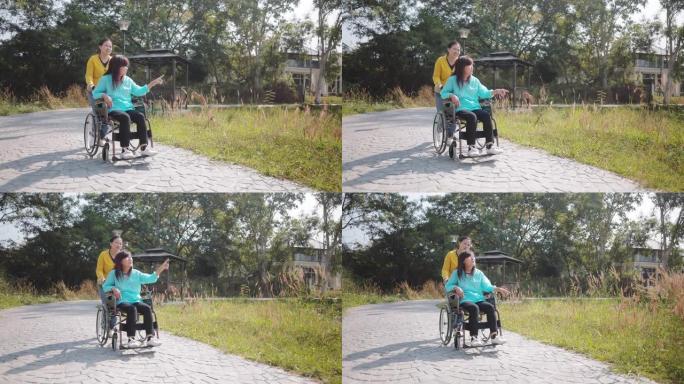 快乐微笑的母亲坐在轮椅上放松和与女儿在公园户外散步