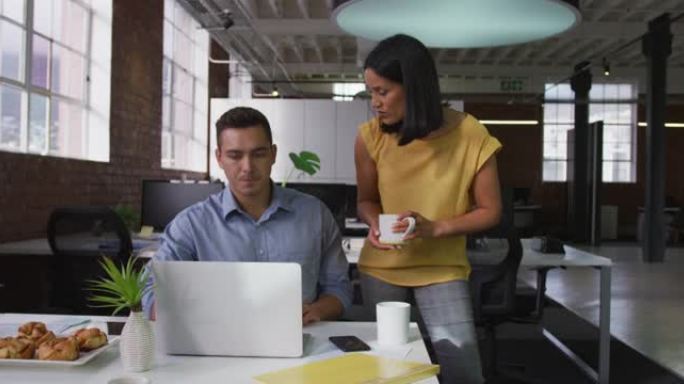 讨论中使用笔记本电脑盛放咖啡的男女商业同事