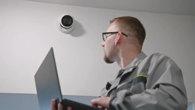穿着制服的安装人员使用笔记本电脑在办公室设置安全摄像头