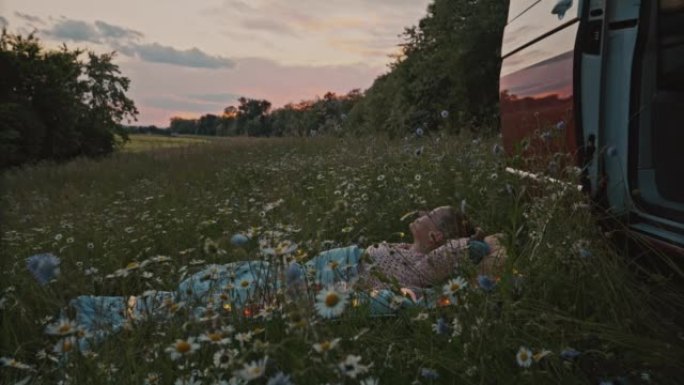 日落时分，DS女人躺在露营车旁边的草地上，使用智能手机