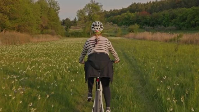 傍晚在乡间小路上骑自行车的金发和头盔的女人，克尔卡国家公园
