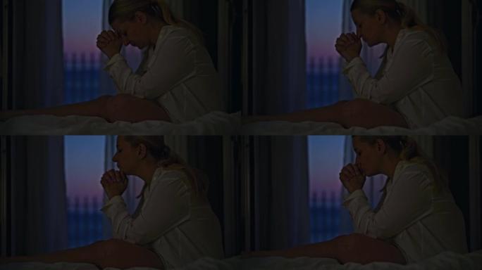 金发女人睡觉前祈祷，晚上坐在酒店房间的床上