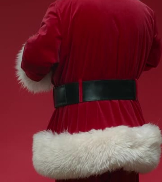 一个在红色背景上转身微笑的圣诞老人，戴着白手套揉着手掌，指着视频结尾的侧面
