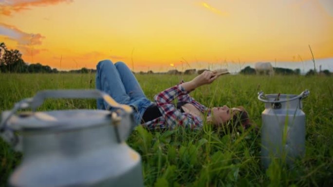 SLO MO Young女牧场主在黄昏时躺在草地上时使用智能手机