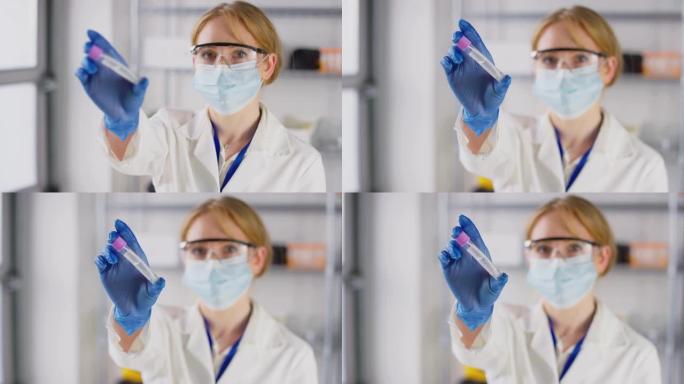 女实验室研究人员戴着安全眼镜和口罩，手持PCR拭子试管