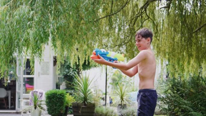 穿着游泳衣的男孩在夏天的花园里用水枪玩得开心