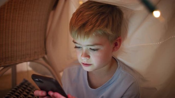 坐在书房或营地里的男孩在家里玩手机