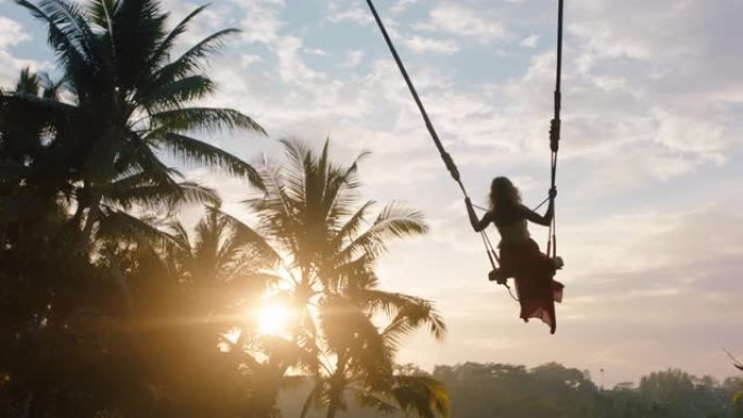 慢动作旅行女人在日出时在丛林中摇摆在热带雨林中摇摆，阳光照耀着棕榈树假日生活方式自由
