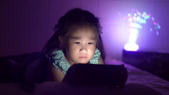 可爱的小女孩晚上在卧室里使用平板电脑