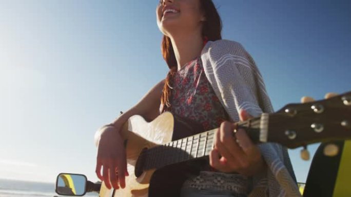 快乐的高加索女人坐在海边的沙滩车里弹吉他