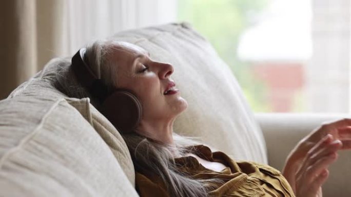 老年女性戴着耳机躺在沙发上听旋律