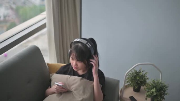 亚洲中国少女用耳机和智能手机躺在垫子上听音乐