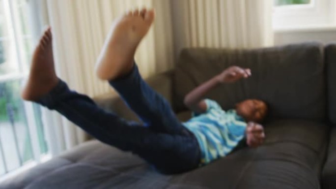 微笑的非洲裔美国男孩在家里的沙发上跳跃