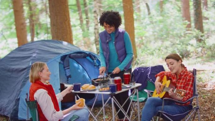 一群女性朋友在森林露营度假时做饭，喝咖啡，他们坐在帐篷旁唱歌，以慢动作拍摄吉他