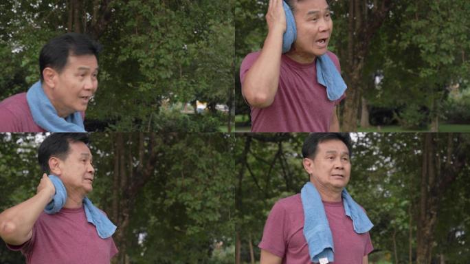 手持镜头: 亚洲高级男子早上在公园跑步后休息。他用毛巾擦干锻炼时的汗水。做瑜伽和太极拳运动后，他累了