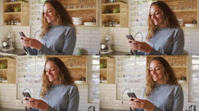 快乐的高加索女人站在阳光明媚的小屋厨房里，用智能手机微笑着