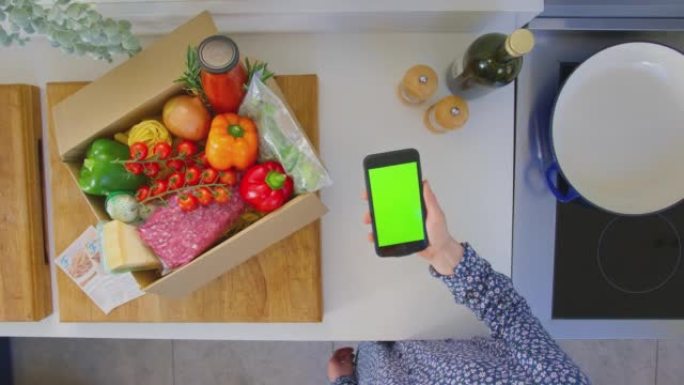 女人在厨房里用新鲜食材在绿屏手机上寻找在线食谱的头顶镜头-慢动作拍摄