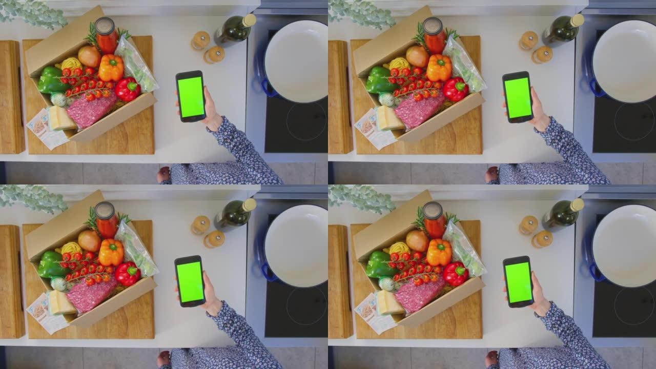 女人在厨房里用新鲜食材在绿屏手机上寻找在线食谱的头顶镜头-慢动作拍摄