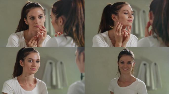 一名年轻的微笑的少女在清洁面部日霜或晚霜后正在使用，以护理浴室镜子后面的皮肤。