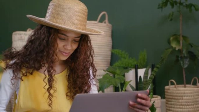使用笔记本电脑对苗圃工作的植物进行研究的年轻女子肖像。黑人女性植物学家在线浏览生态学。花店企业主在互