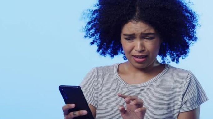 4k视频片段，一个美丽的年轻女子在蓝色背景下使用手机时感到震惊