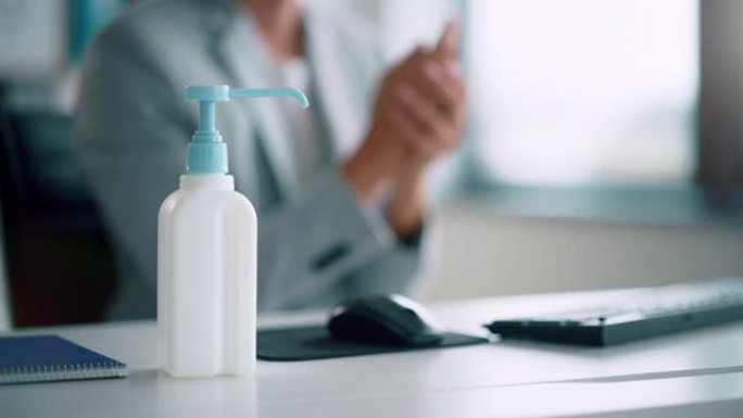 人们在办公室的电脑上在办公桌前工作时使用洗手液。在大流行时期进行健康、安全和卫生建设。专注于战斗