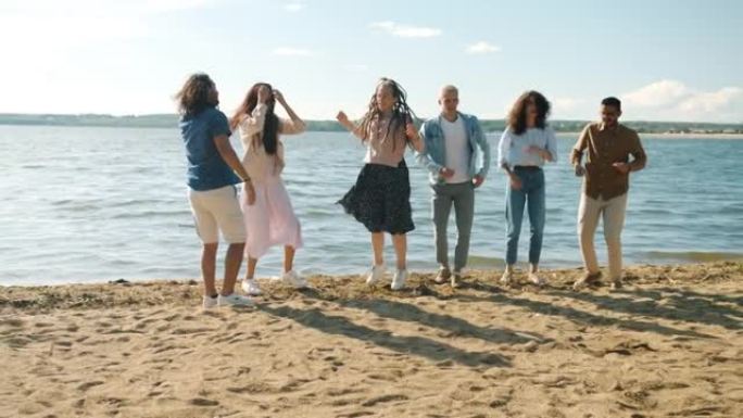 快乐的千禧一代在海滩上跳舞，然后跳起来举起手臂大笑的慢动作肖像