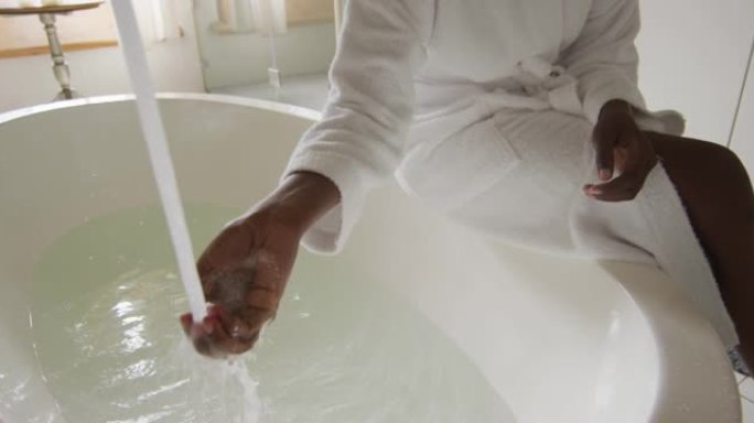 穿着白色长袍的非洲裔美国迷人女人的腹部坐在浴缸上，准备洗澡