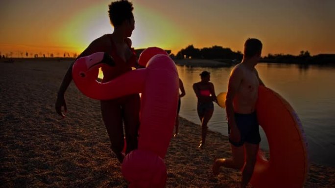SLO MO年轻人在黄昏时带着游泳花车在沙滩上行走