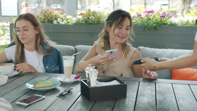 快乐的朋友在露天咖啡馆享受时光，然后在夏天用智能手机付款